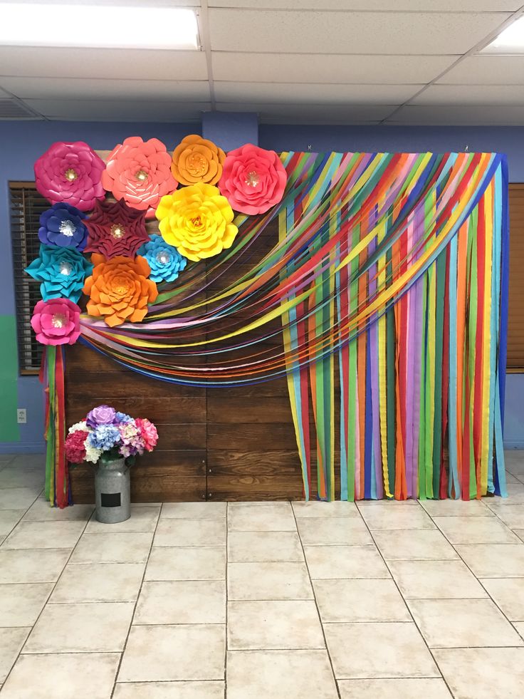 colorful paper flowers are hanging on the wall in front of a backdrop with streamers