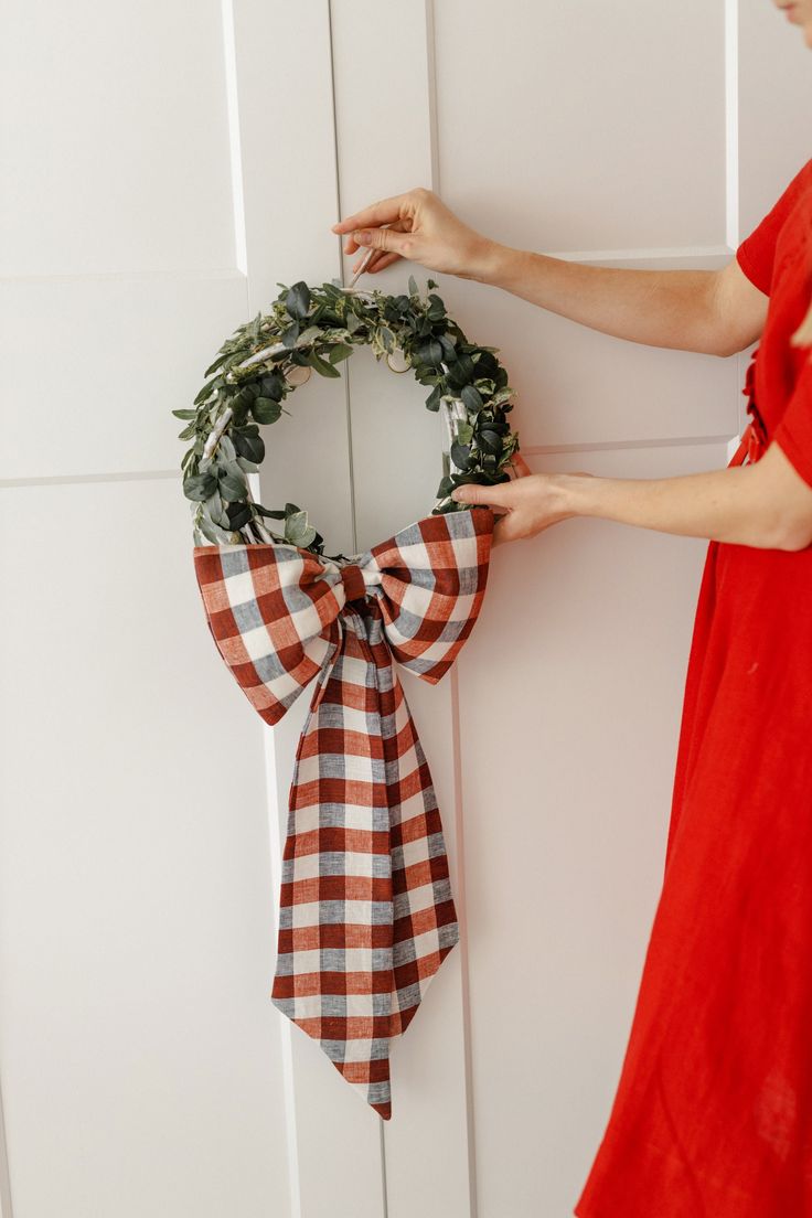 a woman is holding a wreath on the door with a ribbon around it and another person's hand