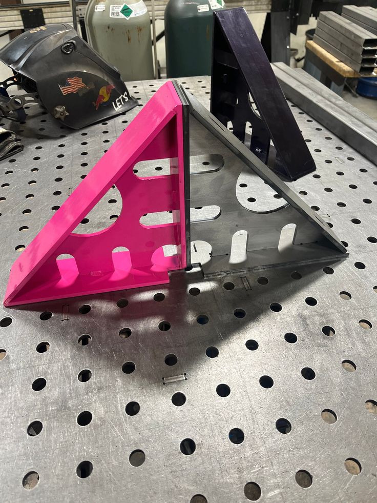 a pink triangle shaped object sitting on top of a metal table with holes in it