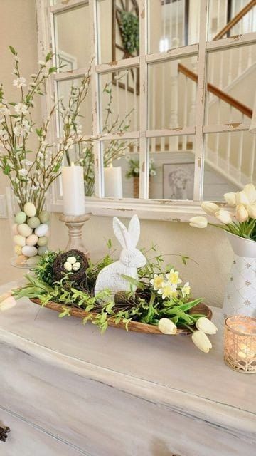 a white dresser topped with lots of flowers and eggs in front of a large mirror