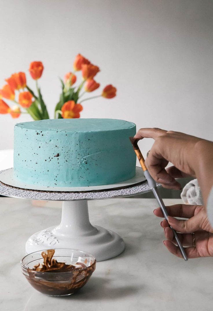 someone is decorating a blue cake with flowers in the back ground and on top of it