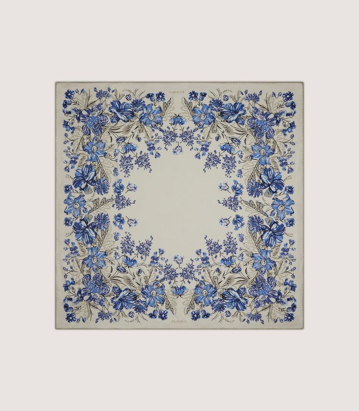 a square blue and white plate with flowers on the border, in front of a gray background