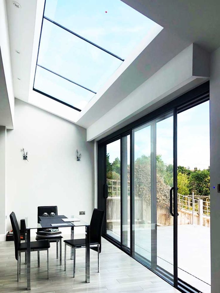 a dining room with glass walls and sliding doors leading to an outdoor patio area that has a skylight above the table