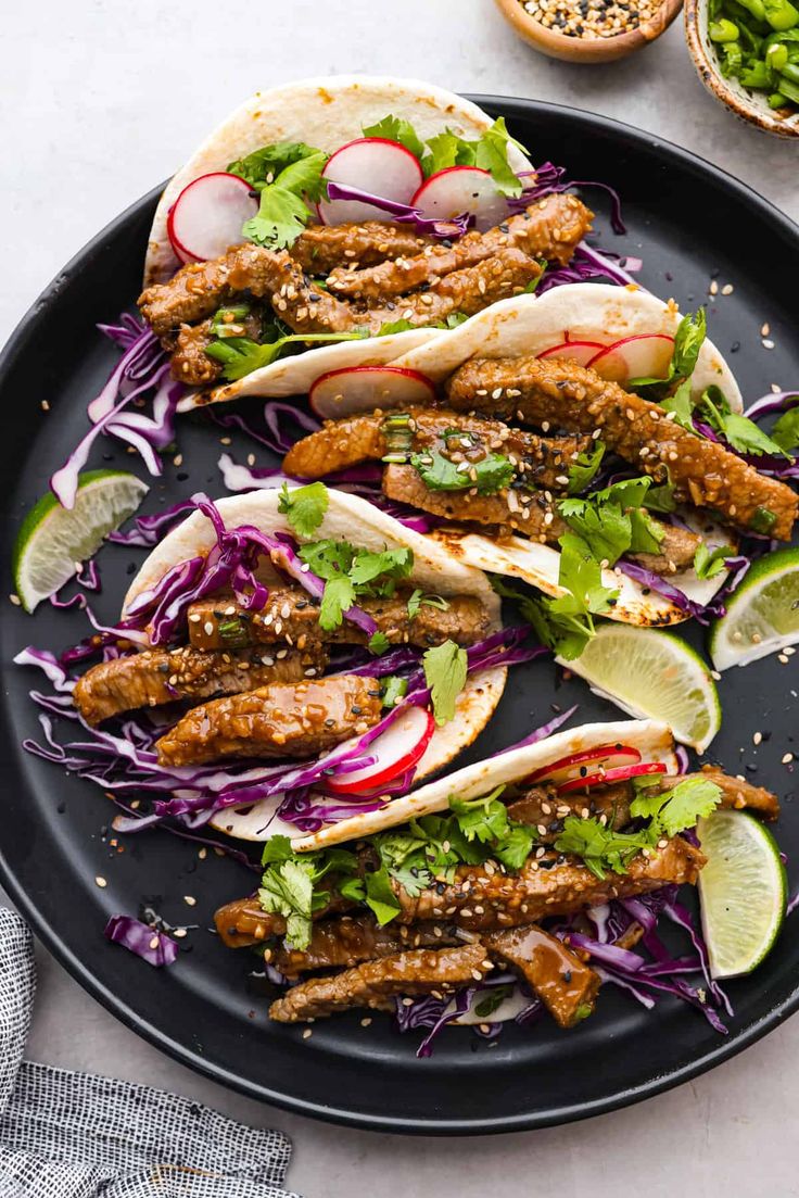 three tacos with meat, cabbage and radishes on a black plate