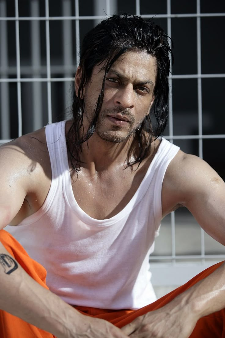 a man with long black hair sitting in front of a cage holding an orange frisbee