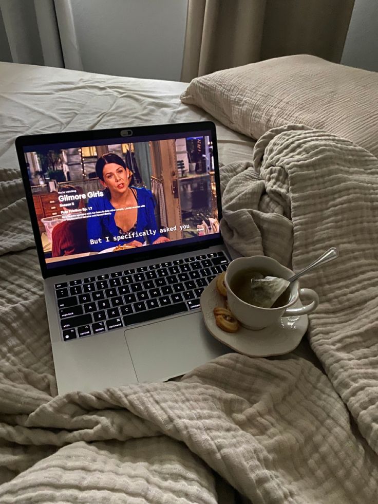 an open laptop computer sitting on top of a bed next to a cup of coffee