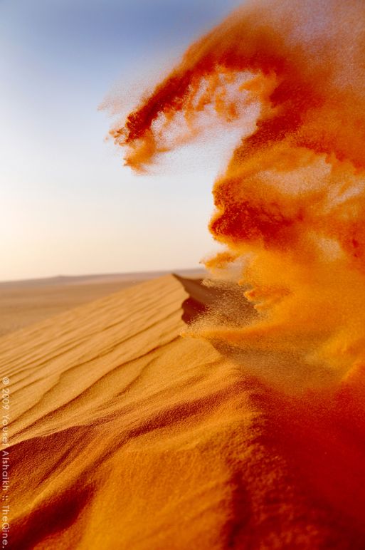 an orange substance is in the air above sand dunes and blue sky with white clouds