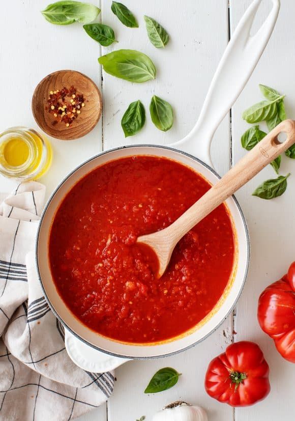 tomato sauce in a pot with basil leaves and garlic on the side next to it