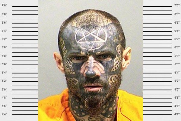 a mug shot of a man with tattoos on his face and chest, wearing an orange shirt