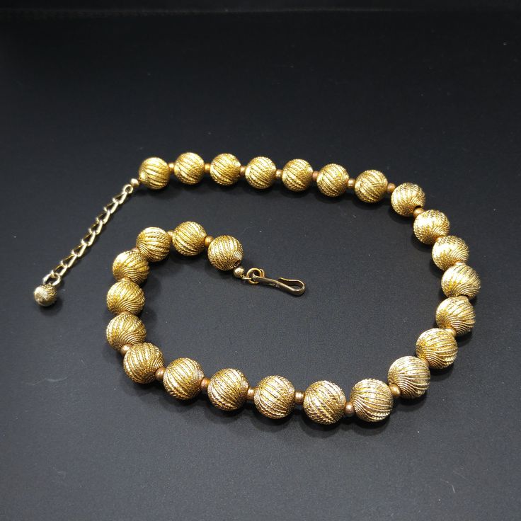 "*Description: This is a beautiful Napier gold tone beaded necklace which is strung on chain from the 1950s. The 12mm beads have a swirling textured finish with smaller spacer beads on the extension chain. This necklace is signed on the hook \"Napier\". This is a great statement necklace for any outfit or make a wonderful vintage jewelry gift. *Approximate Measurements: Length - 17 Inches, Width - 1/2 Inch *Condition: Great vintage condition. Will see signs of wear under magnification. *Hallmark Vintage Gold Jewelry With Large Beads, Vintage Gold Single Strand Jewelry, Vintage Yellow Gold Polished Bead Necklace, Vintage Beaded Necklace With Gold Beads For Formal Occasions, Vintage Formal Beaded Necklace With Gold Beads, Vintage Yellow Gold Necklaces With Polished Beads, Vintage Gold Beaded Necklace For Formal Occasions, Vintage Yellow Gold Necklace With Polished Beads, Gold Necklace With 16 Inch Round Beads