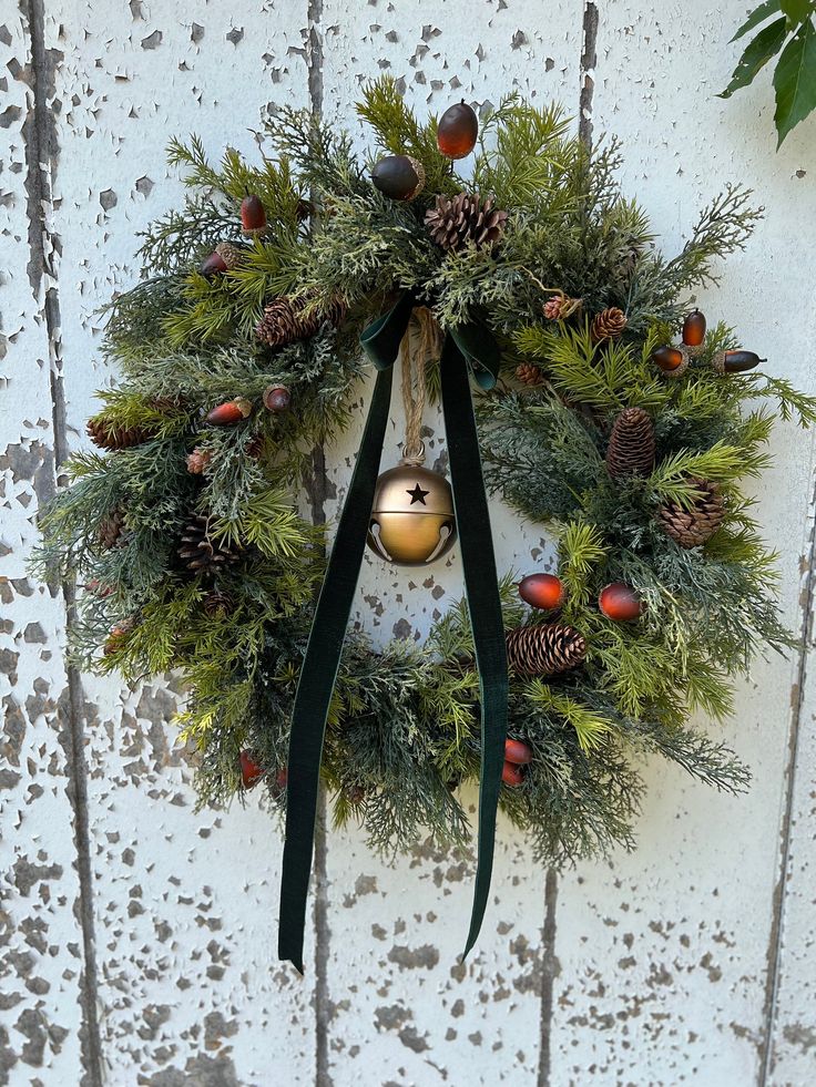 a wreath hanging on the side of a door with pine cones and evergreens around it