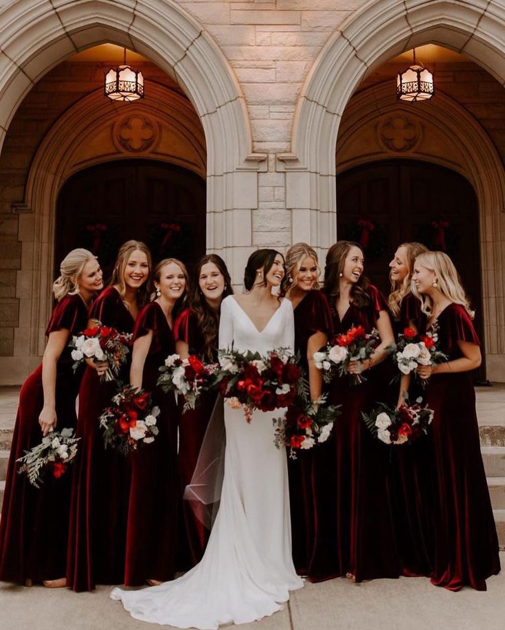 a group of women standing next to each other in front of a building holding bouquets