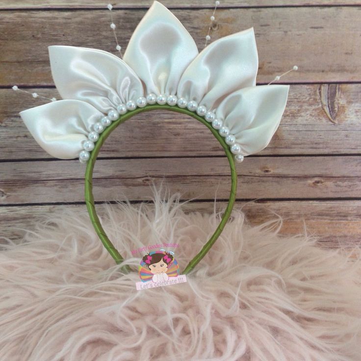 a white flower headband with pearls on it and a bow at the top in front of a wooden background