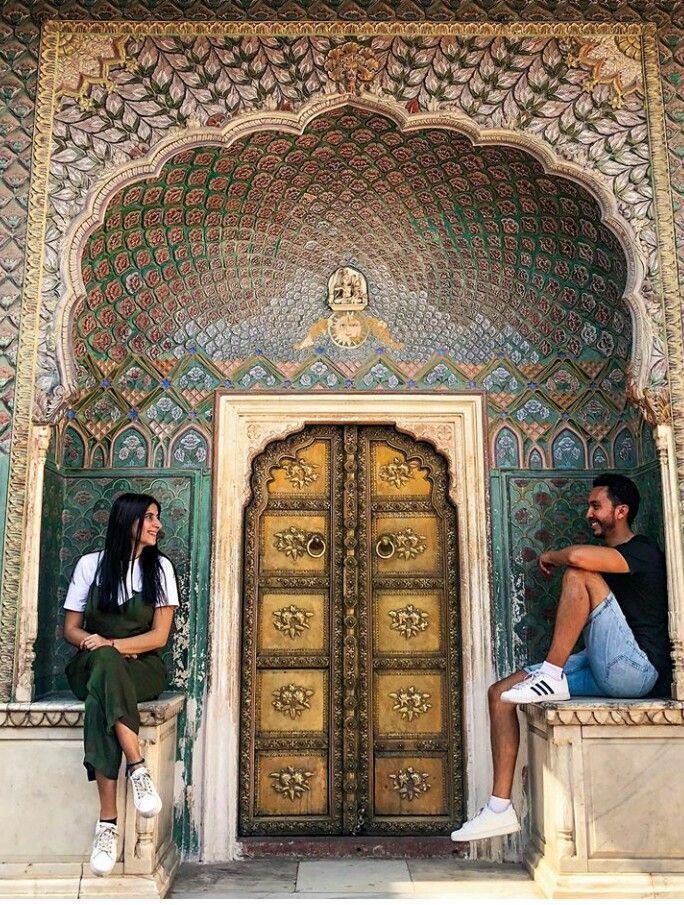 two people sitting on the ledges in front of an ornate building with gold doors