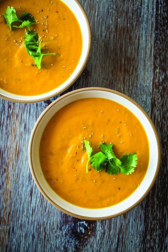 two bowls of coconut ginger carrot soup with cilantro garnish on top