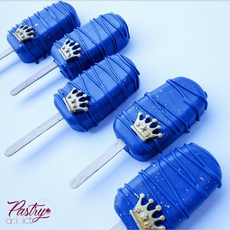 four blue cake pops with gold crowns on them sitting next to each other and two forks sticking out of them