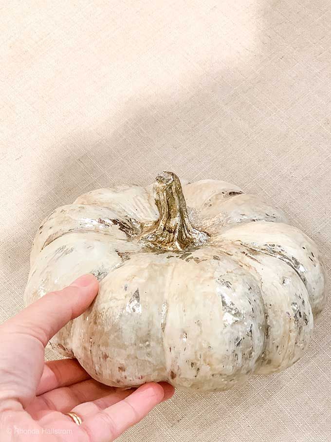 a hand holding a small white pumpkin on top of a table