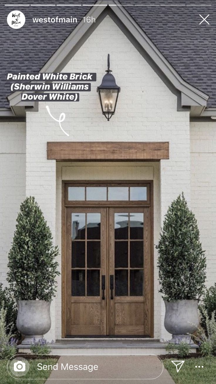 the front entrance to a white brick house with two large planters on each side