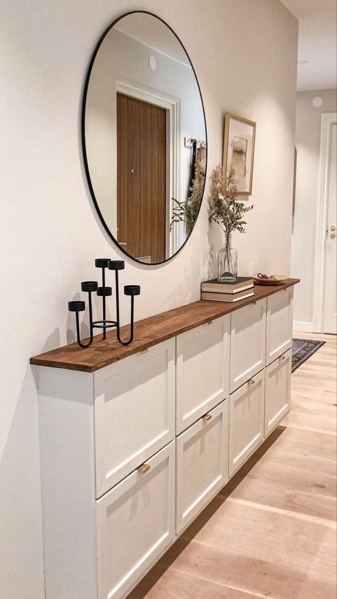 a large mirror is hanging on the wall above a long white cabinet with drawers and hooks