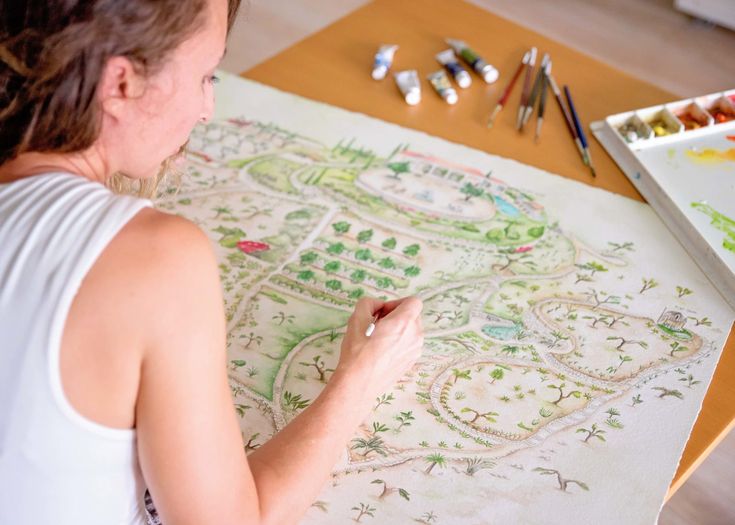 a woman sitting at a table drawing with colored pencils and watercolors on paper