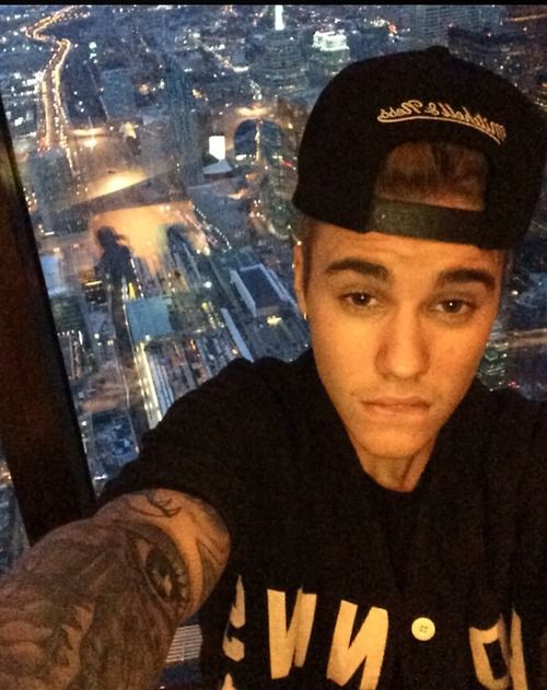 a man in a black shirt and cap sitting at a table with a view of the city