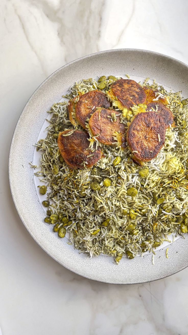 a white plate topped with rice and meat covered in green peas on top of a marble table