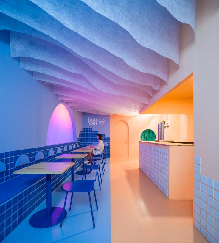 the interior of a restaurant with blue and pink walls, tables and chairs on either side of the counter