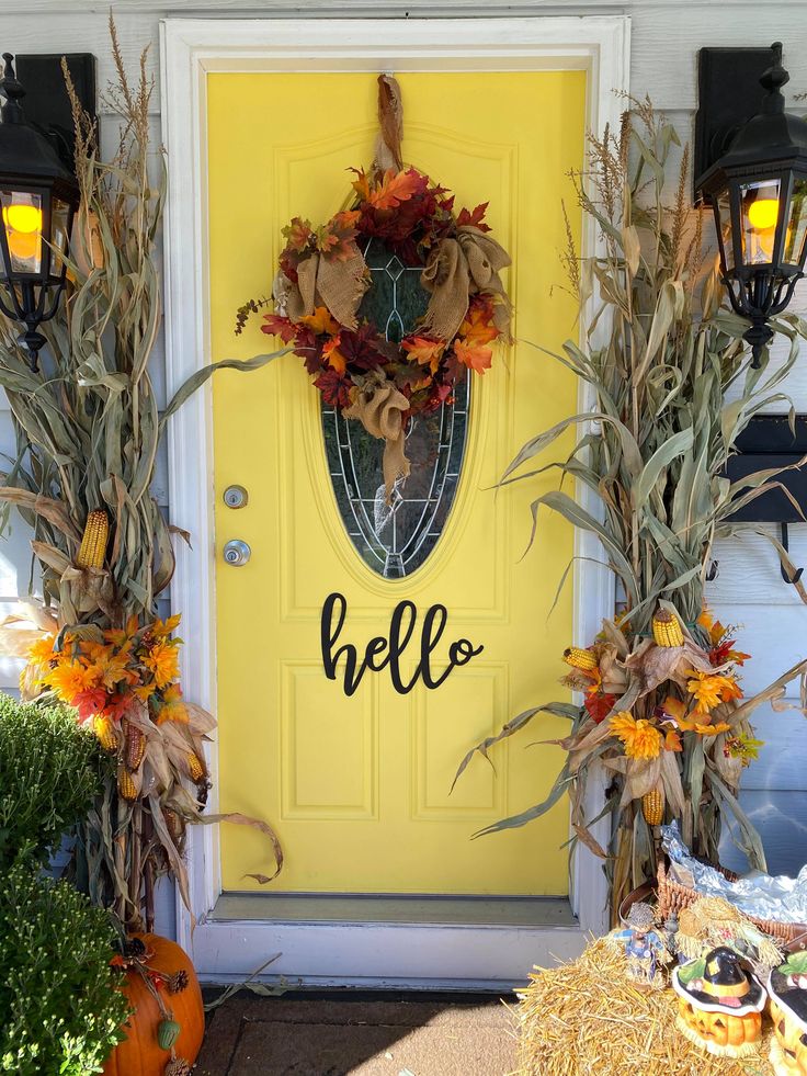 a yellow front door decorated for fall with pumpkins and cornstatch wreaths