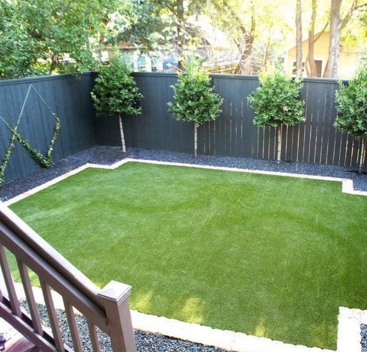 a small backyard with grass and bushes in the back yard, as well as a wooden fence