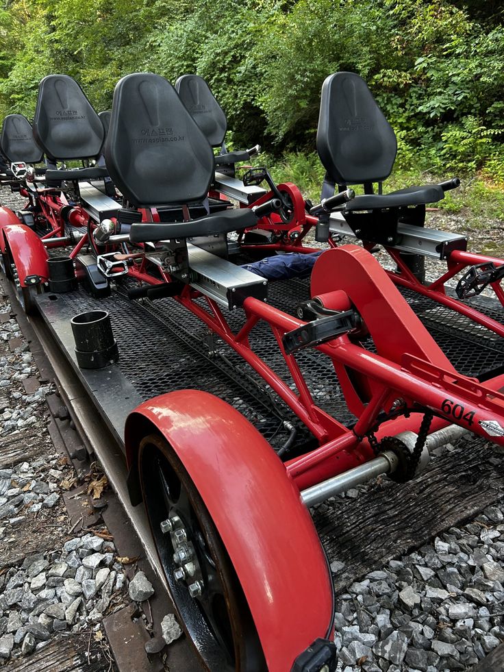 three red pedalbikes are sitting on the back of a train car in front of some trees