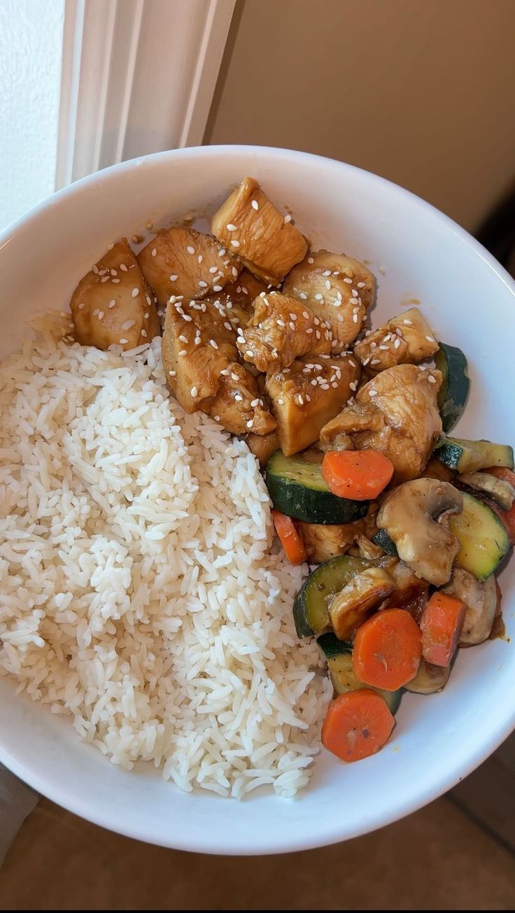 a white bowl filled with rice and veggies covered in sesame seed chicken sauce