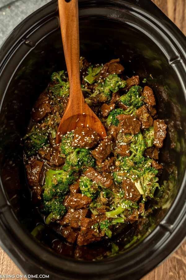 beef and broccoli in a crock pot with a wooden spoon