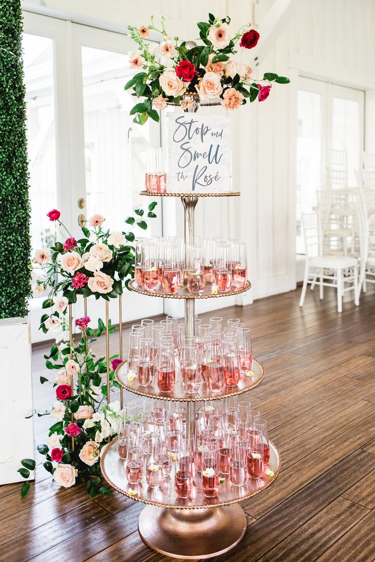 a tiered cake with wine glasses on it and flowers in vases next to it