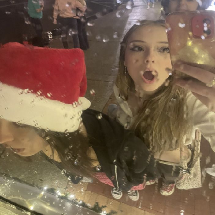 a young woman taking a selfie in front of a christmas hat on the street