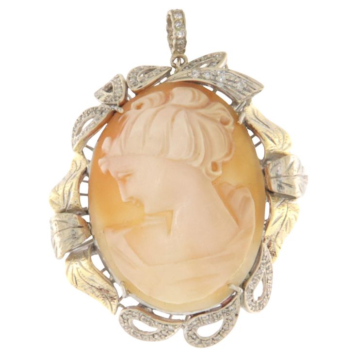 This elegant pendant is a true masterpiece of craftsmanship, made in 18-carat white and yellow gold, set with brilliant-cut diamonds that add an unparalleled touch of radiance. At the center of the pendant, a finely hand-carved cameo stands out, depicting the delicate profile of a classic female figure. The artisanal expertise is evident in the intricate details of the face, hair, and features, which give the cameo an air of grace and refinement—an ancient art deeply rooted in Italian tradition. The cameo setting is surrounded by a white and yellow gold motif, resembling stylized leaves, which adds movement and dynamism to the design of the jewelry. The yellow gold leaves provide a delicate color contrast, further enhancing the central cameo, while the diamonds, carefully arranged along th Gold Motif, Elegant Pendant, Gold Leaves, Female Figure, Cameo Pendant, Yellow Gold Pendants, Face Hair, Color Contrast, Drop Necklace