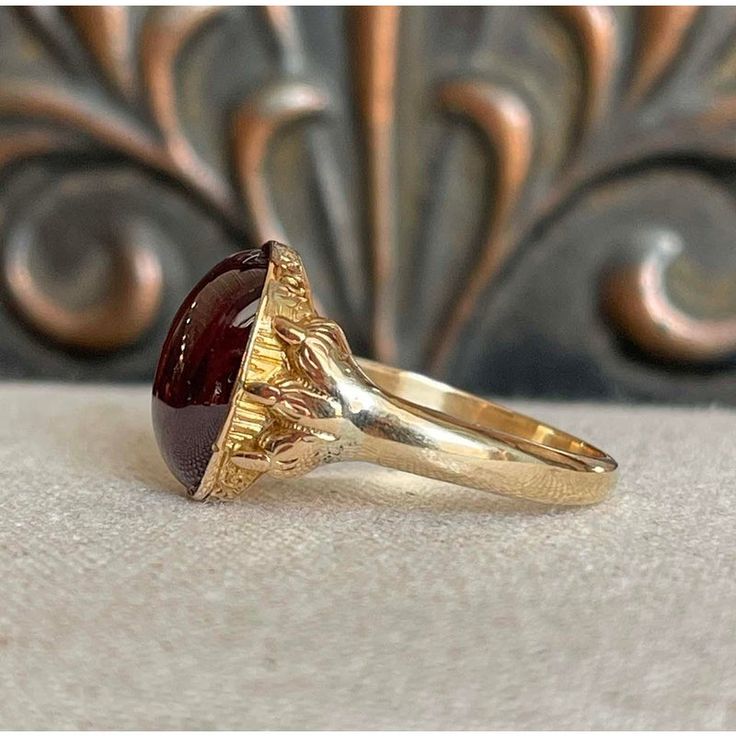 Step back to a time of refined elegance with this Victorian Garnet Signet Ring, a splendid piece that exudes the charm of the early 19th century. This impressive ring features a large cabochon garnet, measuring 14.4x11.5 mm, set in a distinctive signet style. The garnet is closed backed, emphasizing its rich, deep color and classic appeal.  Originally crafted around 1840-50, the ring has been expertly re-shanked; while the top mounting and the intricately detailed clawed feet are made of 15 karat gold, the band itself has been updated with 9 karat gold. Measuring 15.3 mm north to south and 19.3 mm across at the face, the ring sits 6 mm off the finger and narrows to 2.5 mm at the back. Weighing 4.8 grams and sized at 10, this well-loved ring showcases both historical craftsmanship and a tim Formal Domed Signet Ring With Cabochon, Classic Yellow Gold Signet Ring With Cabochon, Classic Red Oval Cabochon Signet Ring, Antique Ruby Signet Ring, Vintage Red Signet Ring With Oval Cabochon, Vintage Red Oval Cabochon Signet Ring, Classic Yellow Gold Cabochons For Formal Occasions, Classic Domed Cabochon Signet Ring, Timeless Cabochon Rings For Formal Occasions