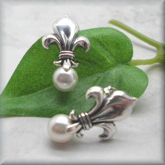 "Sterling silver fleur de lis stud earrings are accented with a glowing white Swarovski elements half-drilled pearl. Classic, beautiful and unusual. This symbol has traditionally been used to represent French royalty, and in that sense it is said to signify perfection, light, and life. Fleur de lis translates to \"flower of the lily\" in English. The earrings are about 7/8\" long (1.8 cm) from the top of the fleur de lis to the bottom of the pearl. Setting, earnuts and earring components are all Classic White Flower Earrings For Pierced Ears, White Classic Flower Earrings For Pierced Ears, Classic White Flower Earrings, White Classic Flower Earrings, Classic Silver Wedding Plug Earrings, Classic Silver Plug Earrings For Weddings, Elegant Silver Flower Clip-on Earrings, Elegant Silver Clip-on Plug Earrings, Classic White Sterling Silver Clip-on Earrings