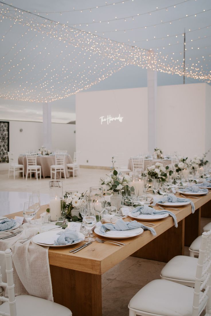 a long table with plates and silverware on it in a room filled with white chairs