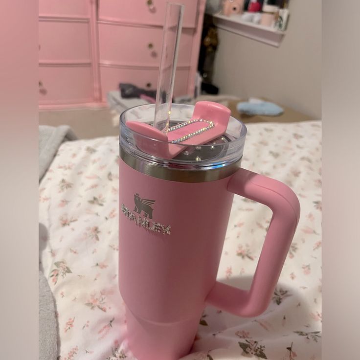 a pink coffee cup with a straw sticking out of it on top of a bed