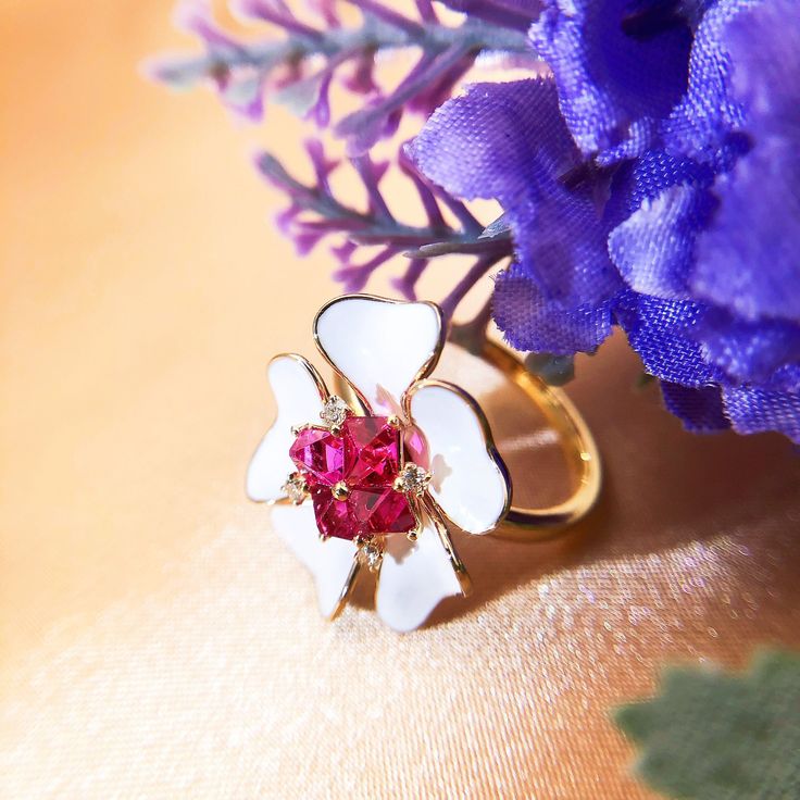 a close up of a ring with a flower on it and purple flowers in the background