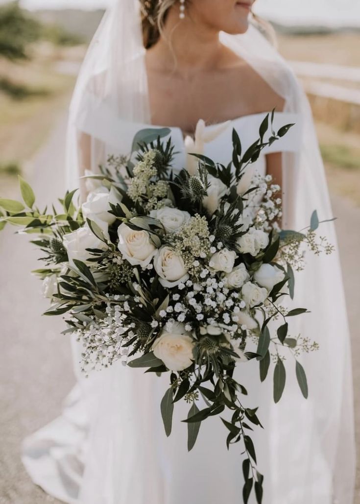 a woman in a wedding dress holding a bridal bouquet with white flowers and greenery