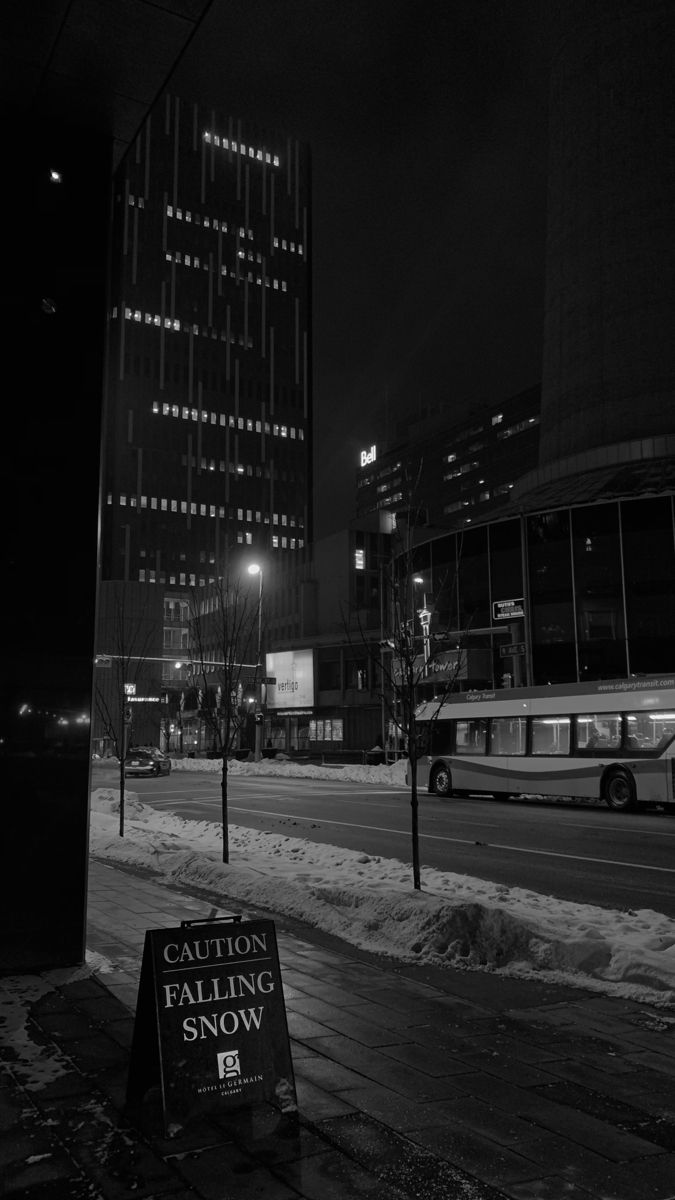 black and white photograph of snow covered street in city at night with bus passing by