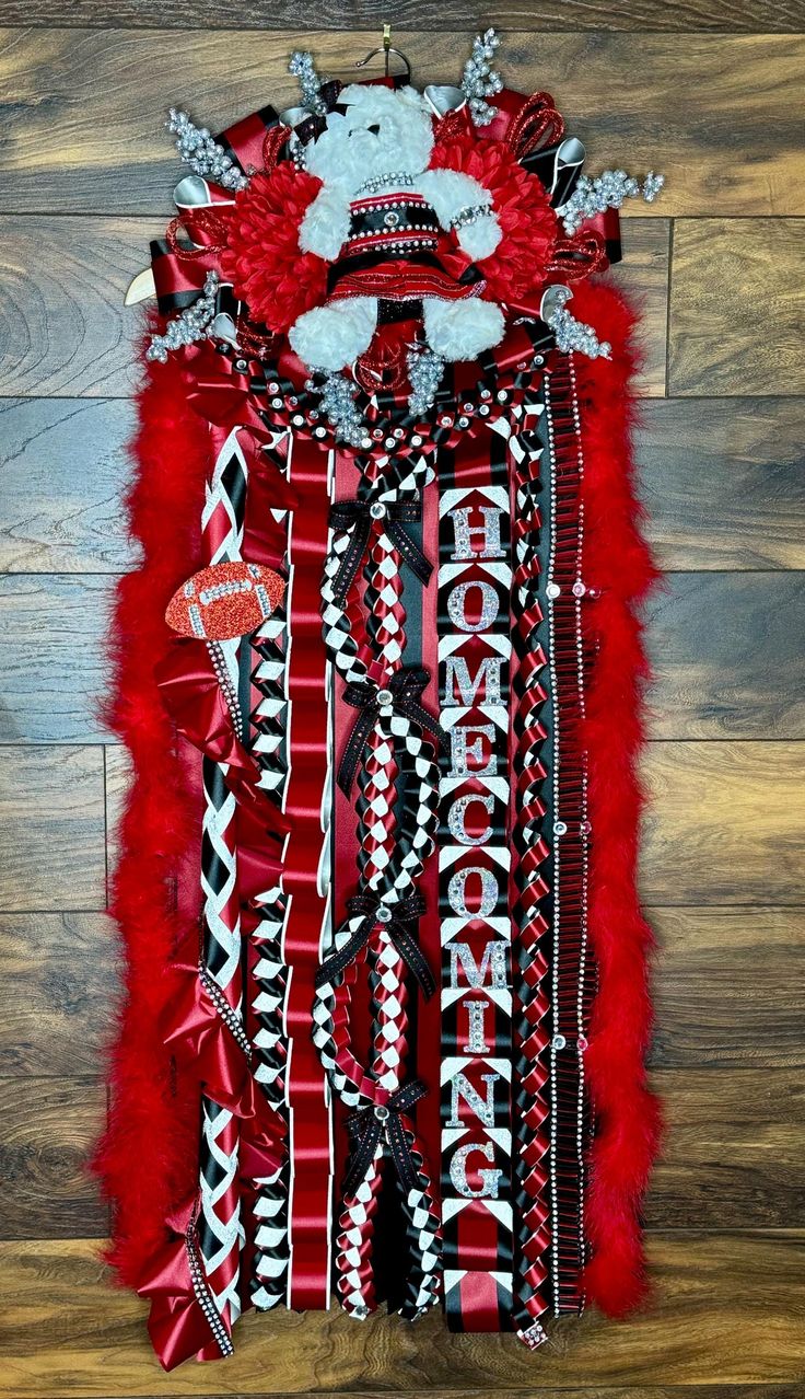 a red and black scarf on top of a wooden floor next to a white teddy bear