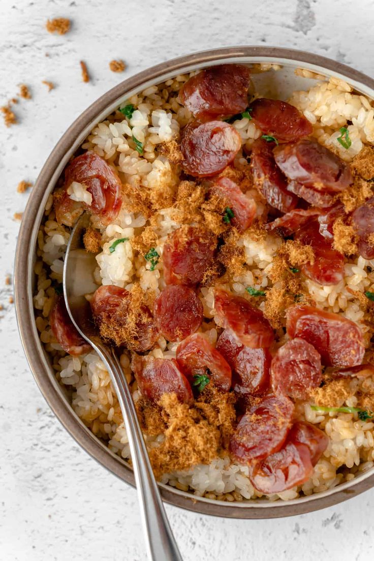 a bowl filled with rice and meat on top of a white countertop next to a spoon