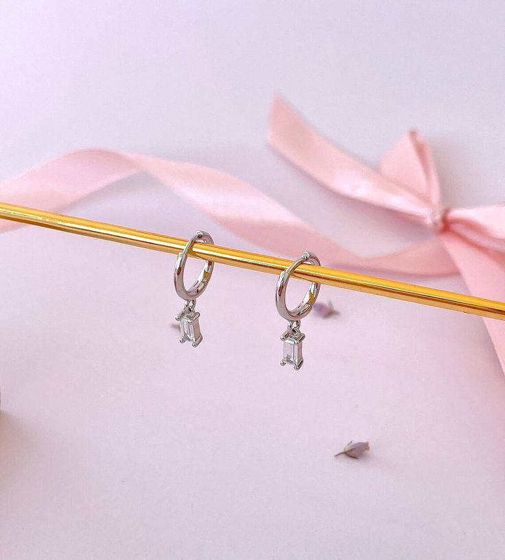 a pair of silver earrings sitting on top of a pink ribbon next to a pencil