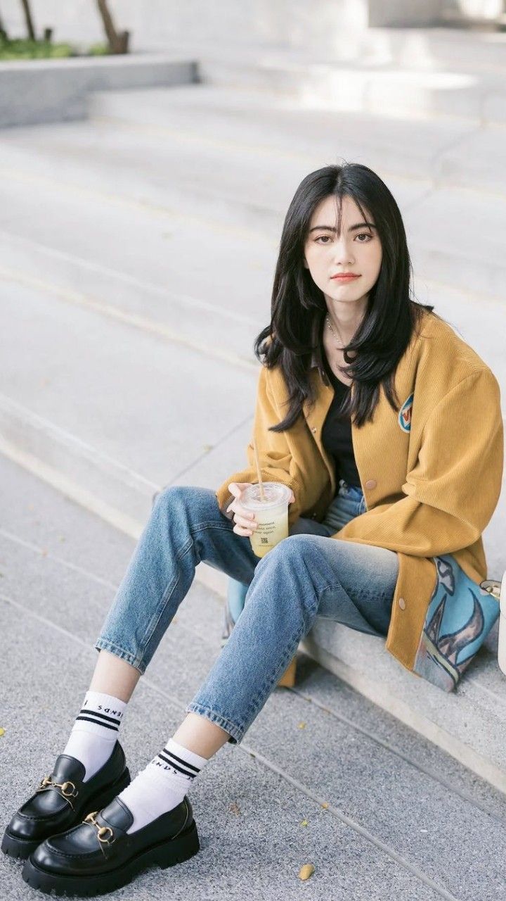 a woman sitting on the ground with her legs crossed and holding a drink in her hand