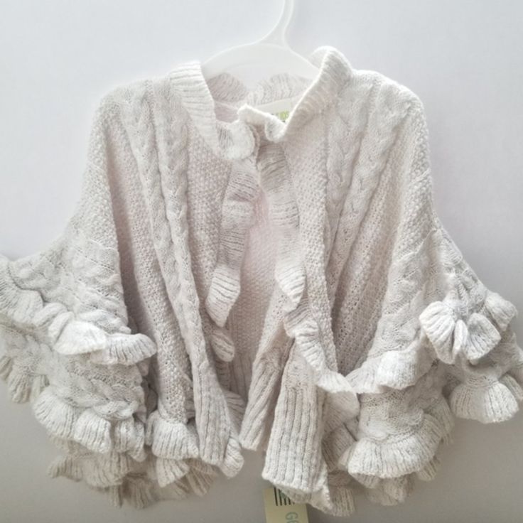 a white sweater with ruffles hanging on a hanger