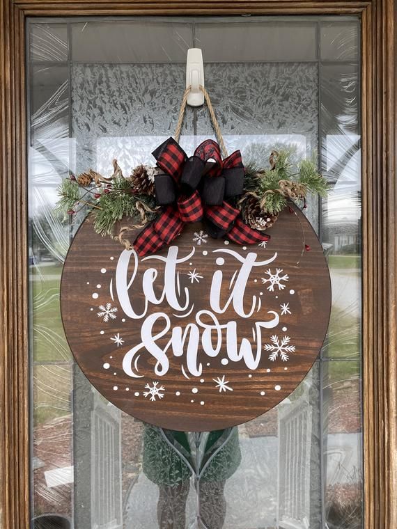 a wooden sign that says let it snow hanging on the front door with a bow