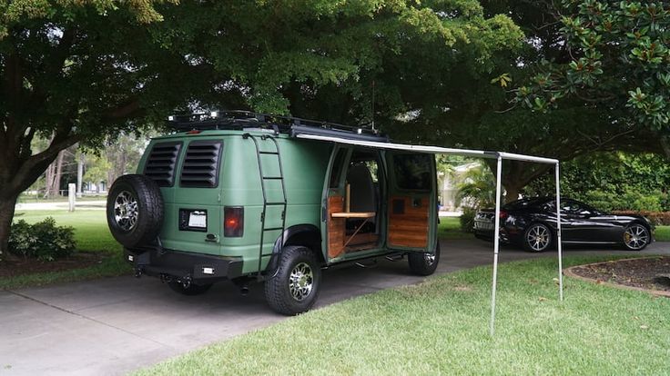 a green van parked in front of a tree next to a car with its door open