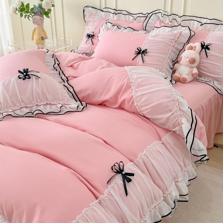 a bed with pink sheets and black ruffles on the bottom, along with a teddy bear